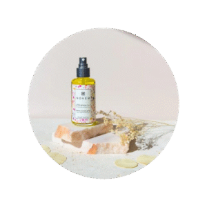 flacon d'huile de jojoba posé sur une pierre rose avec des pétale autour