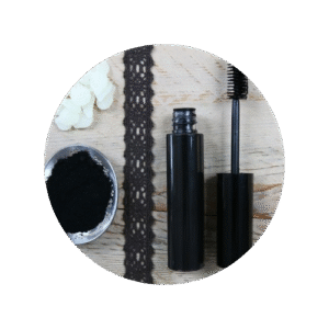 Tube de mascara noir au charbon avec à coté une cuillère remplie de charbon en poudre et une fleure blanche