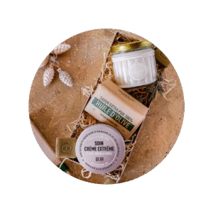 deux pots de baume et de l'huile de jojoba dans une boite rempli de paille avec le couvercle du coffret à coté