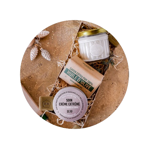 deux pots de baume et de l'huile de jojoba dans une boite rempli de paille avec le couvercle du coffret à coté